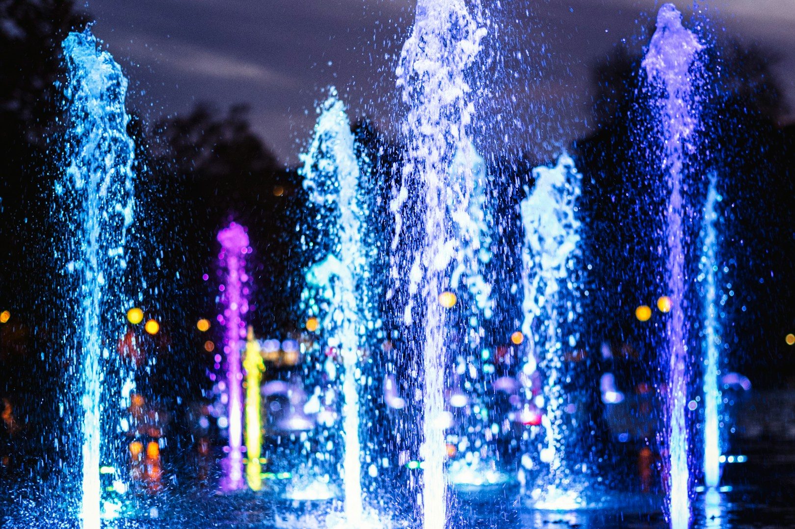 Bunte Wasserfontänen leuchten bei Nacht in verschiedenen Farben.