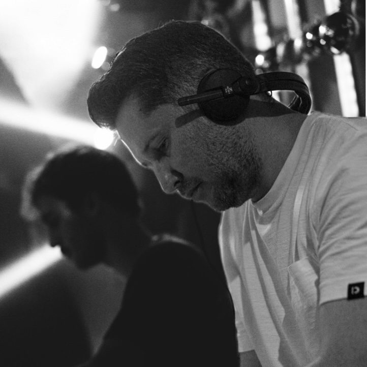 DJ bei einer Aufführung, konzentriert mit Kopfhörern, Lichtstrahlen im Hintergrund.