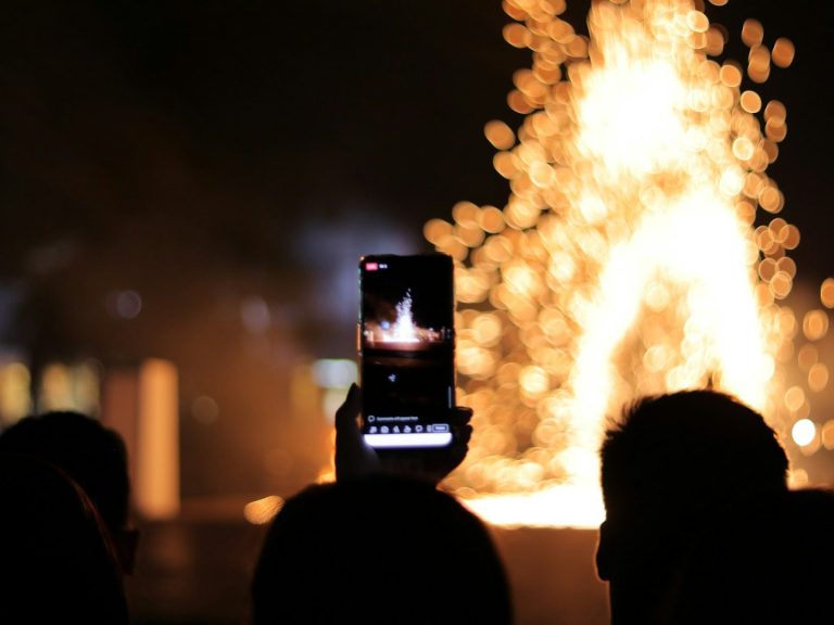 Eine Person hält ein Handy, um ein Feuerwerk bei Nacht zu filmen.