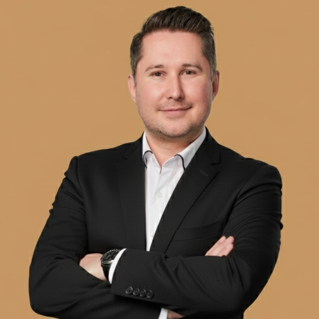 Mann in Anzug mit verschränkten Armen, lächelt freundlich in die Kamera.