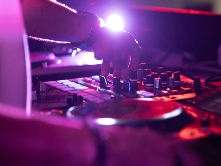 DJ bedient ein Deck mit bunten Lichtern im Hintergrund.